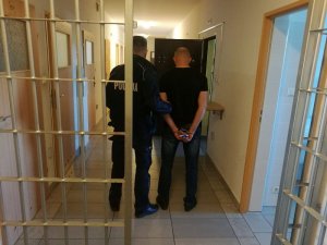 Policjant prowadzi do celi zatrzymanego mężczyznę