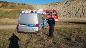 Policjant na żwirowni, obok stoi radiowóz a dalej wóz strażacki