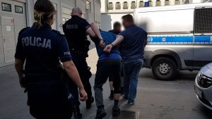 Policjanci prowadzą zatrzymanego do radiowozu,