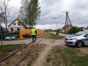 Radiowóz, w tle policjant pracujący na miejscu wypadku drogowego