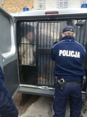 Policjant zamyka kratę od radiowozu.