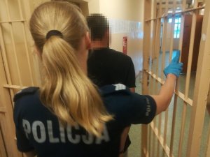 Policjantka prowadzi zatrzymanego do celi