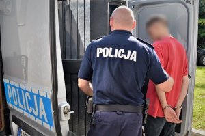 Policjant prowadzi zatrzymanego do radiowozu