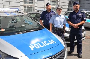 Policjantka stoi z dwoma polskimi policjantami przy radiowozie