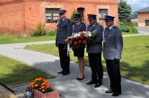 Policjanci stoją z wiązanką kwiatów i oddają hołd poległym