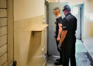 Policjant prowadzi zatrzymanego do celi