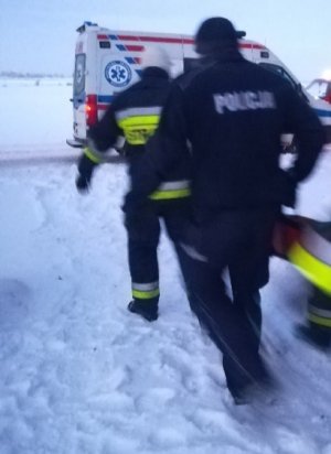 Policjant i strażak wynoszą poszkodowanego na noszach