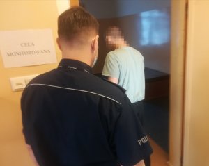 Policjant prowadzi zatrzymanego do celi