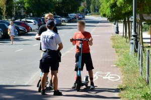 policjant stoi na chodniku obok niego mężczyzna na hulajnodze