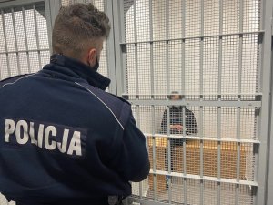 policjant stoi przed celą w której siedzi zatryzmany mężczyzna