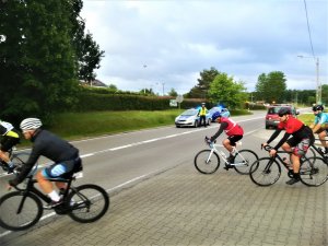 rowerzyści przejeżdżają przez trasę wyścigu, w tle widać oznakowany policyjny radiowóz