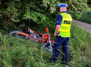 policjant przeprowadza oględziny motocykla, który leży w rowie