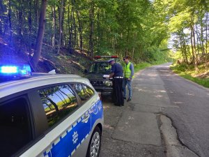 policyjny radiowóz stoi przy jezdni, niedaleko stoją policjanci