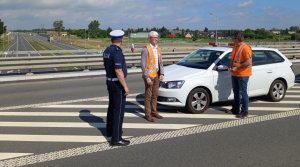 policjant i członek komisji rozmawiają przy radiowozie