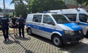 dwóch policjantów prowadzi zatrzymanego przy radiowozie