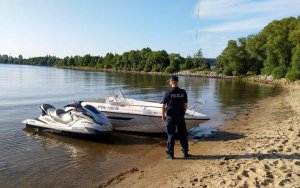 policjant przy brzegu jeziora, w tle motorówka i skuter wodny