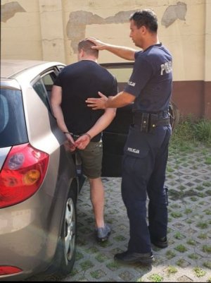 policjant pomaga wsiąść zatrzymanemu do radiowozu