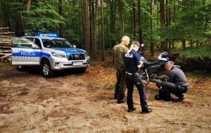 policjanci i strażnik leśny rozmawiają na terenie lasu stojac przy radiowozie