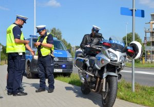 policjanci ruchu drogowego stoją przy  radiowozach i motocyklu