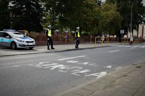 Policjanci stoją w pobliżu przejścia dla pieszych i szkoły