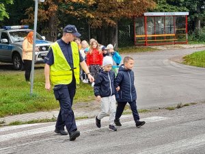 Policjant pokazuje dzieciom w jaki sposób bezpiecznie poruszać się przy szkole