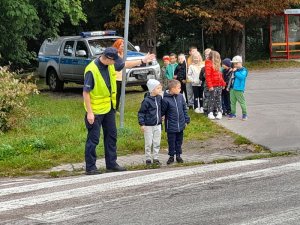 Policjant pokazuje dzieciom w jaki sposób bezpiecznie poruszać się przy szkole