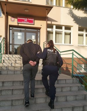 policjant wprowadza do budynku komisariatu zatrzymanego mężczyznę