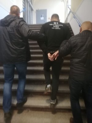 policjanci prowadzą zatrzymanego mężczyznę po schodach