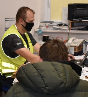 policjant pisze na komputerze za biurkiem siedzi osoba przesłuchiwana przez policjanta