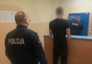 zatrzymany stoi w PDOZ, a za nim stoi policjant