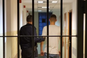 policjant za kratą stoi z zatrzymanym mężczyzną