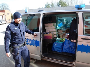 policjant stoi przy radiowozie w którym są dary dla  uchodzćów