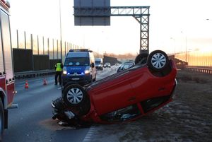 leżący na dachu samochód, policjanci pracujący na miejscu zdarzenia