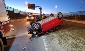 leżący na dachu samochód, policjanci pracujący na miejscu zdarzenia