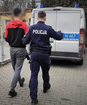 policjant prowadzi do radiowozu zatrzymanego mężczyznę