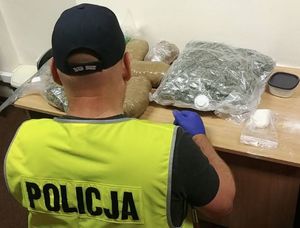 policjant siedzi przy biurku na  którym leżą zabezpieczone narkotyki