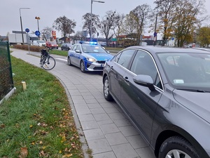 radiowóz stojący na jezdni obok niego stoi rower