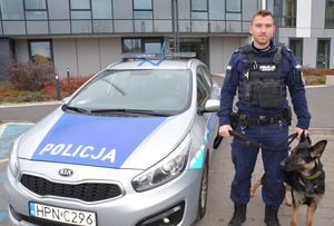 policyjny radiowóz i stojący policjant z psem służbowym