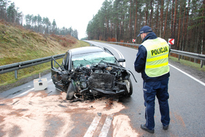 policjant stoi przed uszkodzonym samochodem