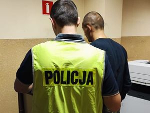 policjant stoi za zatrzymanym mężczyzną