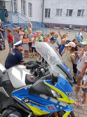 policjantki prowadzą zajęcia z dziećmi, dzieci oglądają  motocykl i zapoznają się z materiałami profilaktycznymi i wspólnie pozują do zdjęcia