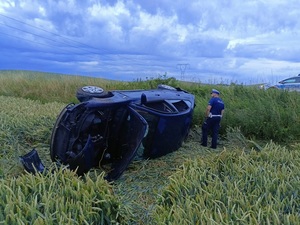 leżące na dachu auto obok stoi policjant