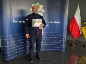 Policjant trzymający dyplom na tle baneru pomorskiej Policji