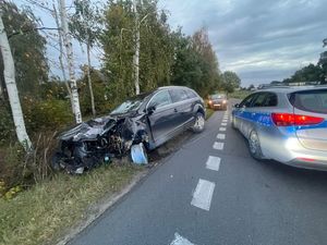 rozbity samochód, który wjechał do rowu obok niego na jezdni stoi oznakowany policyjny radiowóz