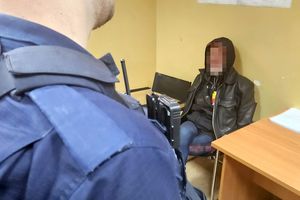 policjant patrzy na zatrzymanego mężczyznę, który siedzi przed nim na krześle. Widok zza pleców policjanta.