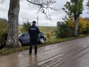 zanieczyszczona droga widać na niej błoto, przy jezdni stoi radiowóz oraz policjant