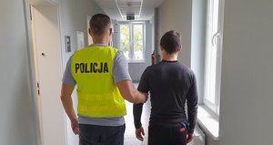 policjant prowadzi przez korytarz zatrzymanego mężczyznyę