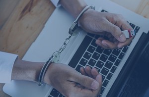 dłonie w kajdankach nad laptopem