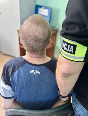 Zatrzymany siedzi na krzesle obok stoją policjanci