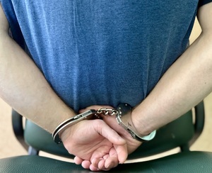 Zatrzymany siedzi na krzesle obok stoją policjanci